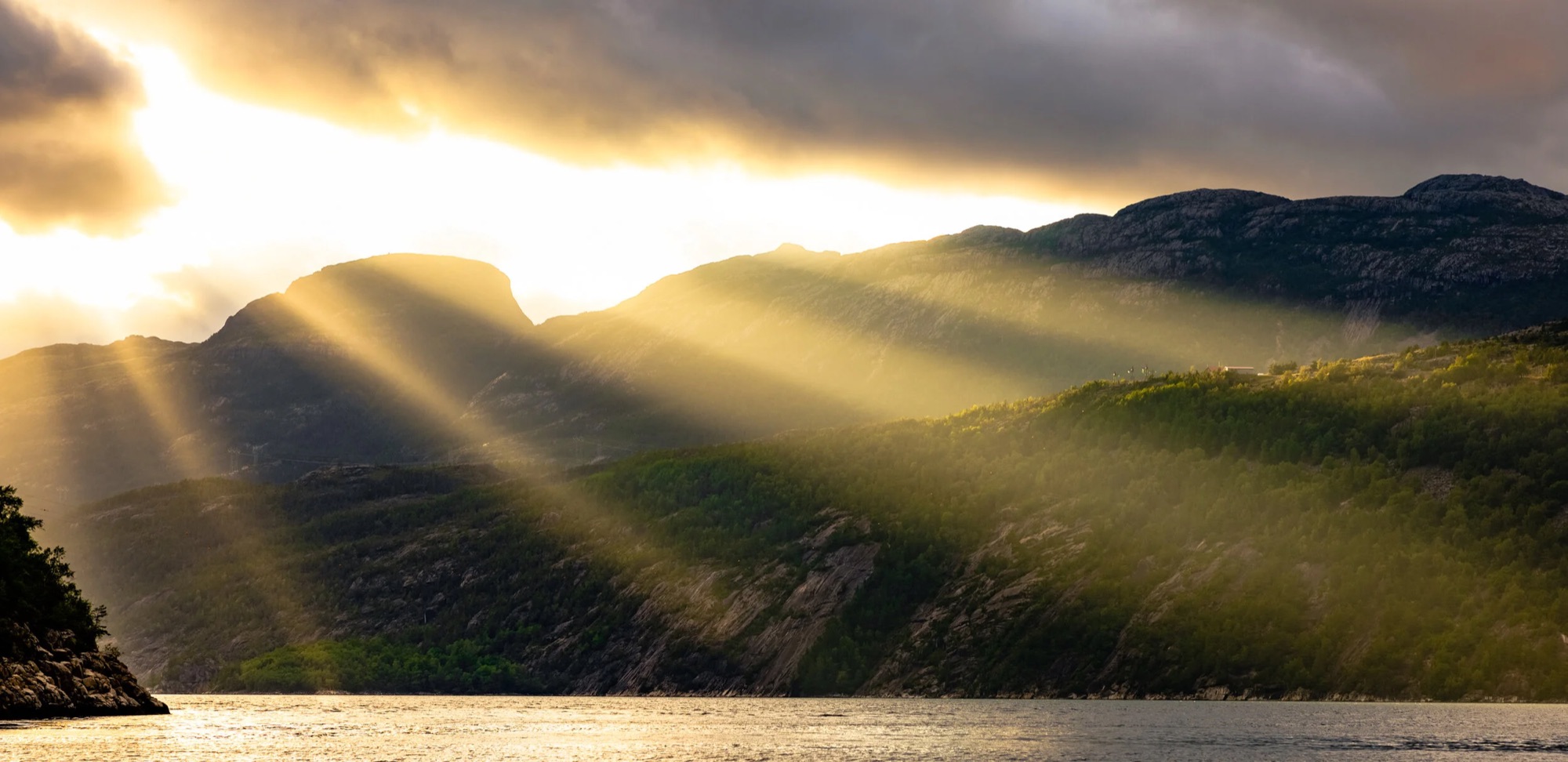 Sollys gjennom skyer over fjell og fjord